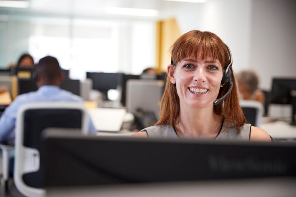 Young woman working at computer with headset in busy office